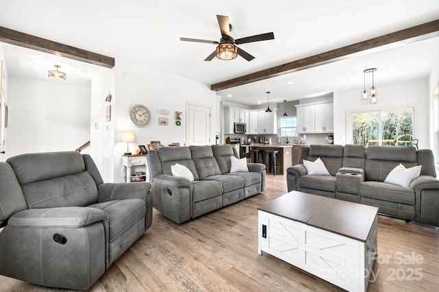 living room with beamed ceiling, light wood-style flooring, and a ceiling fan