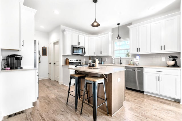 kitchen featuring stainless steel appliances, light countertops, visible vents, white cabinets, and a kitchen bar