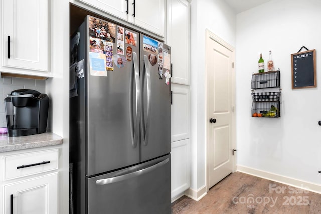 kitchen with baseboards, light wood-style flooring, freestanding refrigerator, white cabinetry, and backsplash