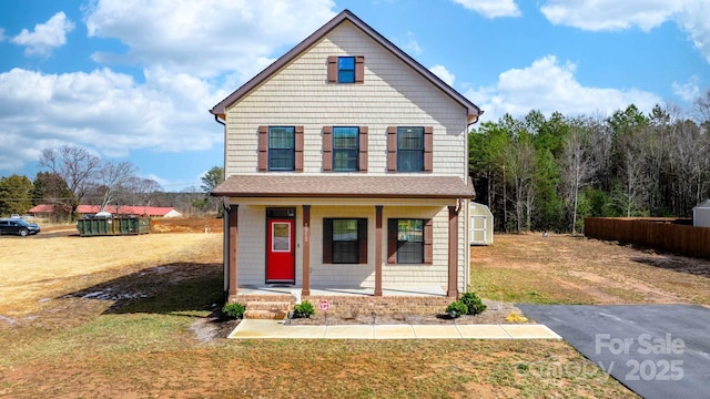 traditional-style home featuring covered porch, a shed, a front yard, and an outbuilding