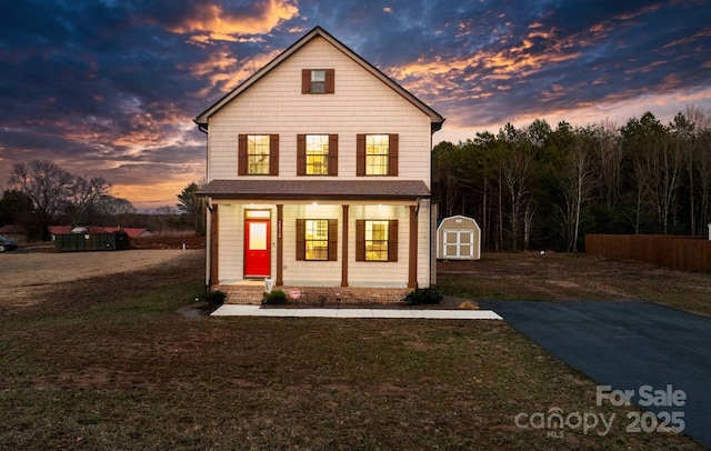 traditional-style home featuring an outbuilding, a porch, a front lawn, and a shed