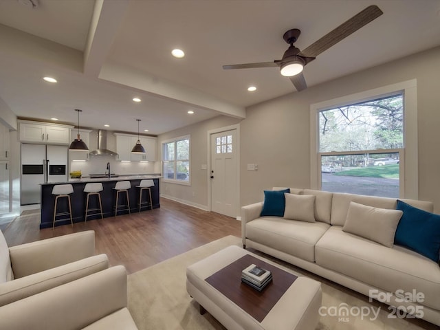 living room featuring beamed ceiling, ceiling fan, sink, and light wood-type flooring