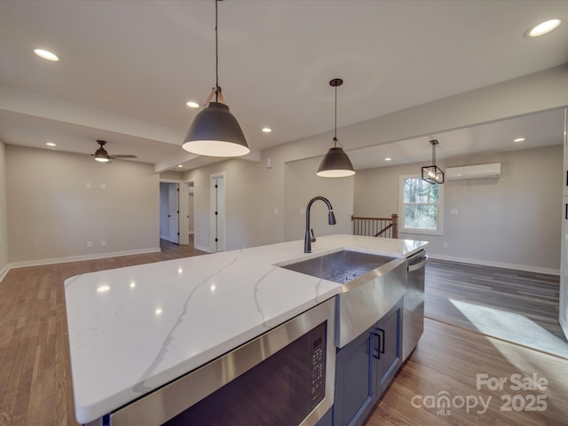 kitchen with pendant lighting, sink, a wall mounted AC, light stone countertops, and a center island with sink