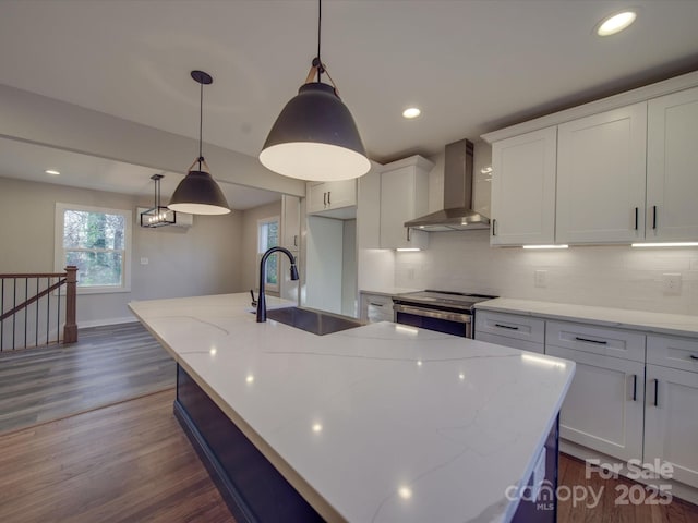 kitchen featuring wall chimney range hood, hanging light fixtures, sink, and stainless steel electric range oven