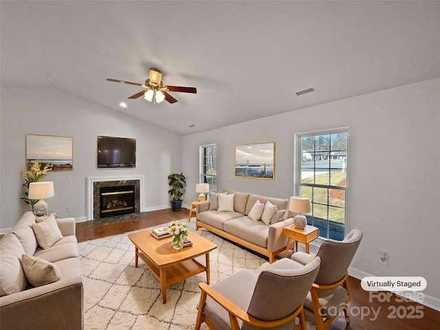 living area featuring visible vents, a ceiling fan, lofted ceiling, light wood-style flooring, and a premium fireplace