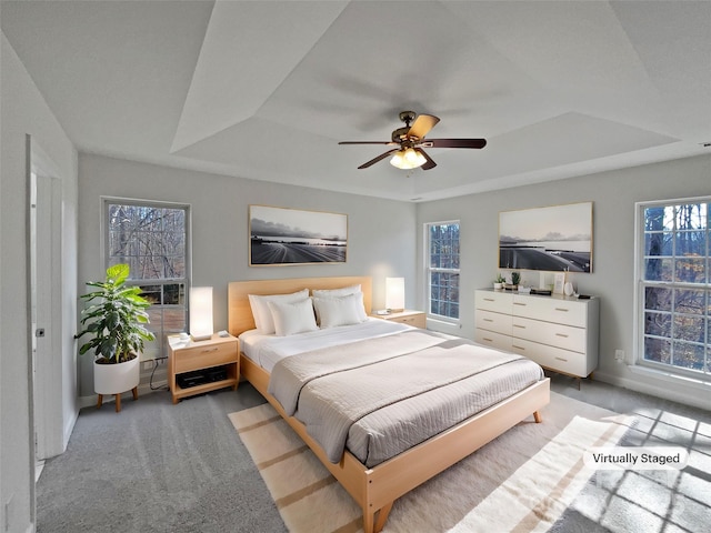 carpeted bedroom with ceiling fan and a raised ceiling