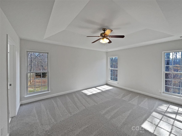 carpeted spare room with ceiling fan, a tray ceiling, and a wealth of natural light