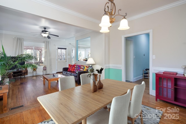 dining room with crown molding, wood finished floors, and ceiling fan with notable chandelier