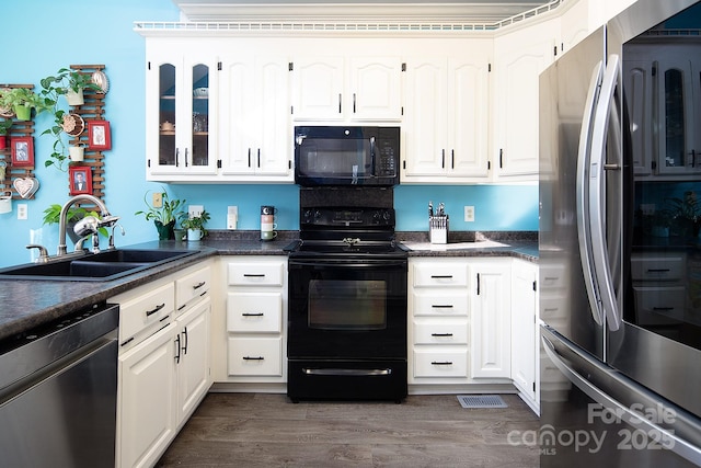 kitchen featuring dark countertops, glass insert cabinets, dark wood-style flooring, black appliances, and a sink