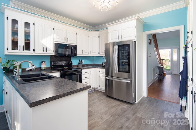 kitchen with dark countertops, a peninsula, light wood-type flooring, black appliances, and a sink