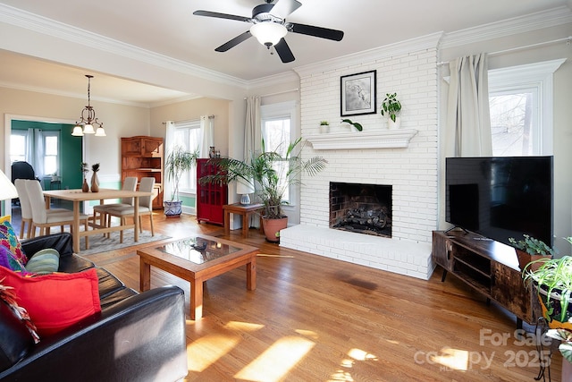 living area with a fireplace, wood finished floors, a ceiling fan, and crown molding