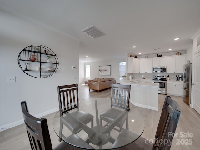 dining room featuring light wood-type flooring, ornamental molding, and sink