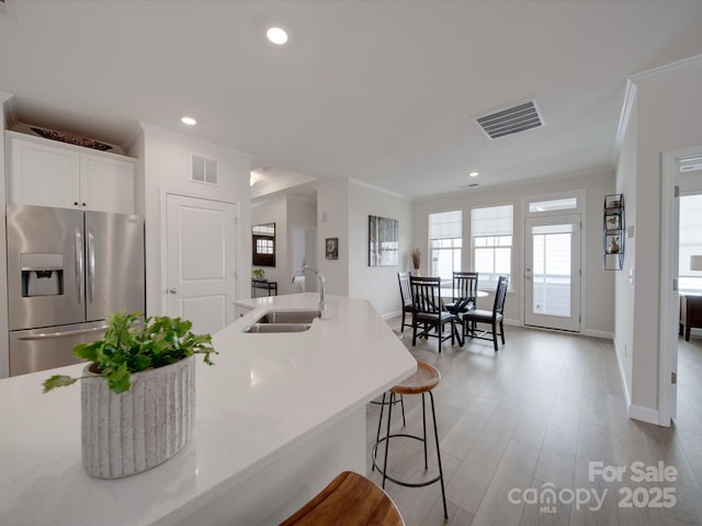 kitchen with white cabinetry, stainless steel refrigerator with ice dispenser, sink, ornamental molding, and a breakfast bar area