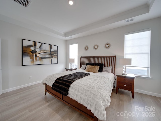 bedroom featuring light hardwood / wood-style floors, a tray ceiling, multiple windows, and ornamental molding