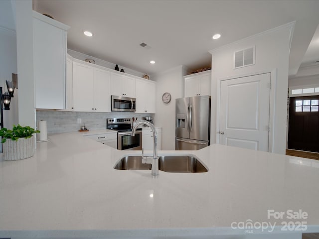 kitchen featuring kitchen peninsula, stainless steel appliances, sink, backsplash, and white cabinets