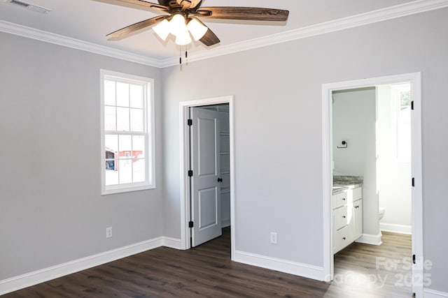 unfurnished bedroom featuring a closet, a walk in closet, ensuite bathroom, crown molding, and dark wood-type flooring