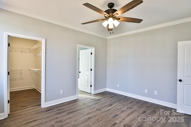 unfurnished bedroom with ceiling fan, crown molding, dark hardwood / wood-style floors, and a spacious closet