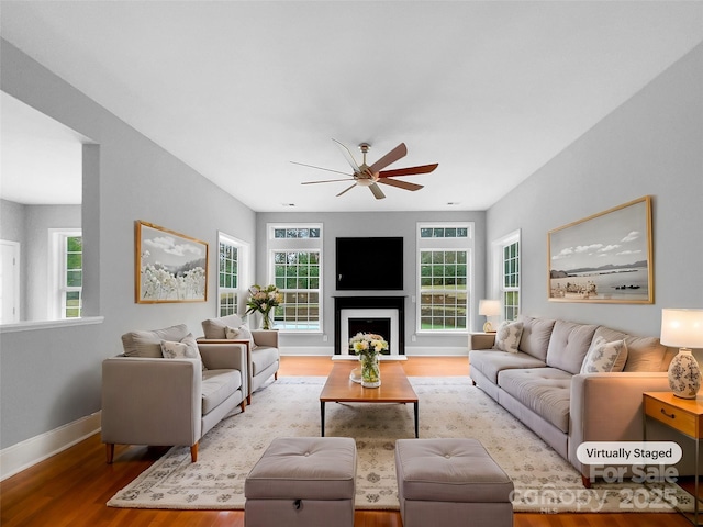 living room with a ceiling fan, a fireplace, baseboards, and wood finished floors