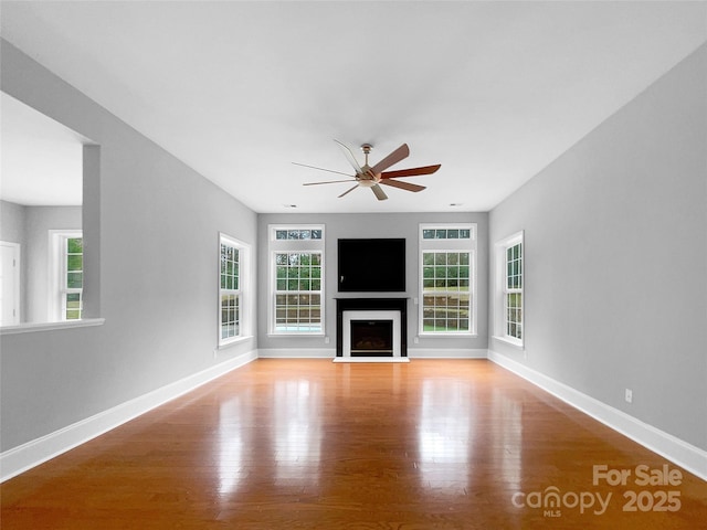 unfurnished living room featuring a fireplace with flush hearth, baseboards, ceiling fan, and light wood finished floors