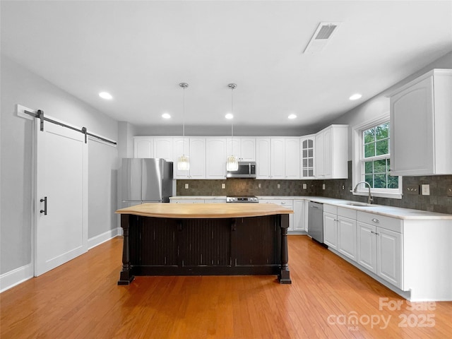 kitchen with a barn door, a kitchen island, glass insert cabinets, decorative light fixtures, and stainless steel appliances