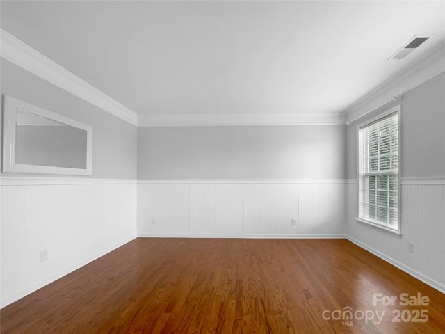 unfurnished room with a wainscoted wall, dark wood-type flooring, ornamental molding, and visible vents