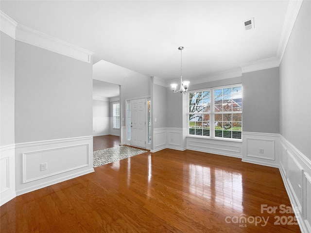 unfurnished dining area featuring a chandelier, a wealth of natural light, a wainscoted wall, and wood finished floors