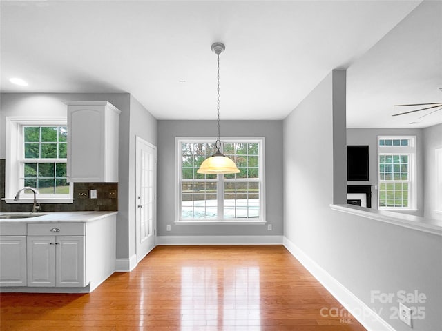 unfurnished dining area featuring ceiling fan, light wood finished floors, a sink, and baseboards