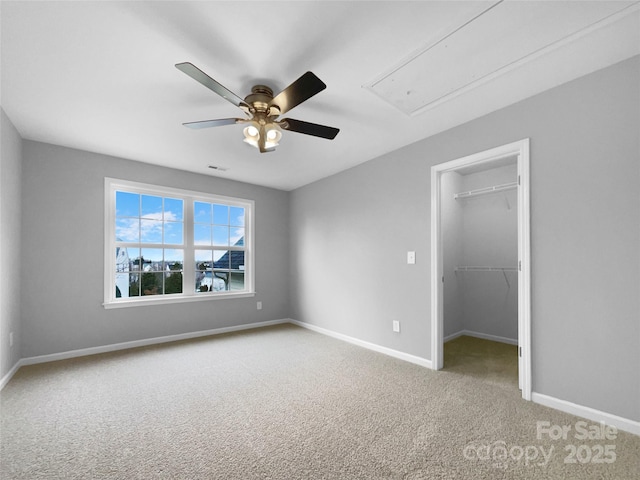 unfurnished bedroom with a walk in closet, a ceiling fan, attic access, light carpet, and baseboards