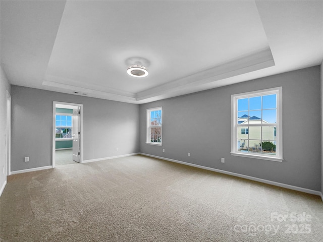 empty room featuring carpet floors, a raised ceiling, and baseboards