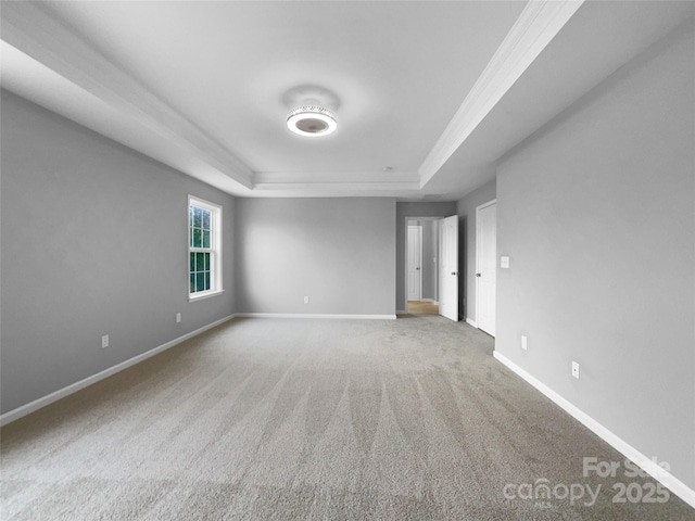 spare room with a tray ceiling, carpet, and baseboards