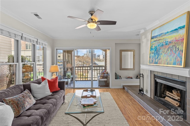 living area featuring ornamental molding, a tiled fireplace, wood finished floors, and visible vents