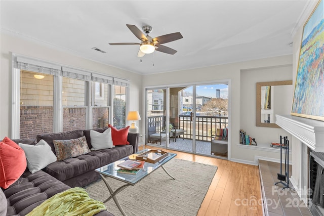 living area with a fireplace, light wood finished floors, visible vents, a ceiling fan, and baseboards