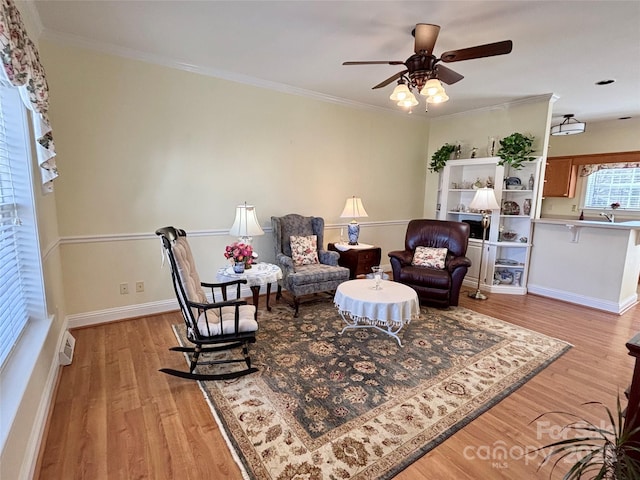 living area featuring ceiling fan, ornamental molding, and light wood-type flooring