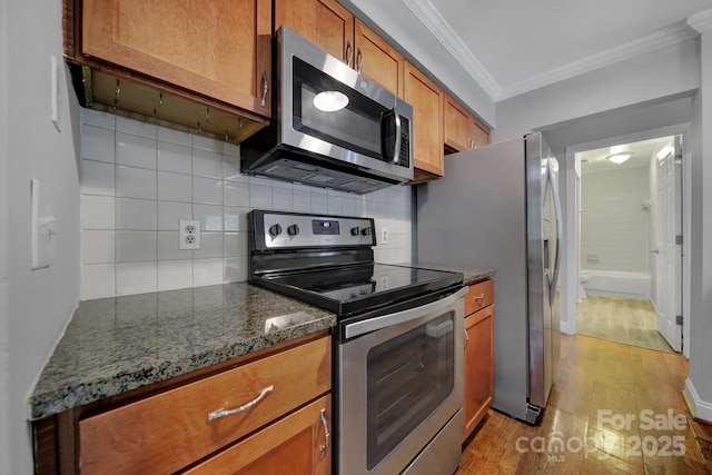 kitchen with tasteful backsplash, ornamental molding, appliances with stainless steel finishes, and dark stone counters