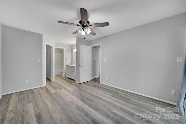 unfurnished bedroom featuring a walk in closet, light hardwood / wood-style flooring, ensuite bath, and ceiling fan