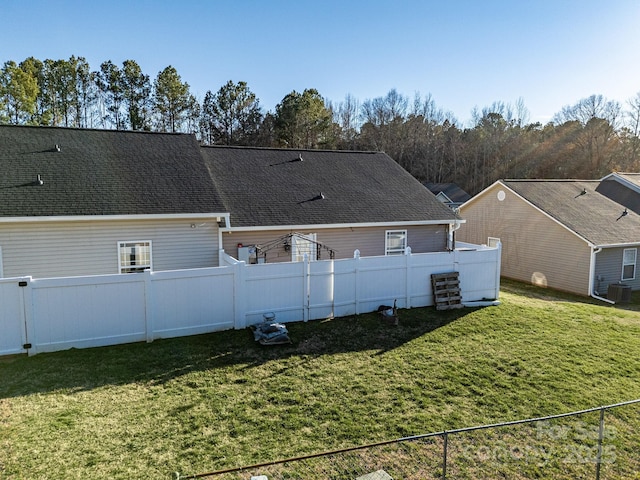 back of house with a fenced backyard, a yard, and roof with shingles