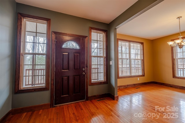 foyer entrance with a chandelier, wood-type flooring, visible vents, and baseboards