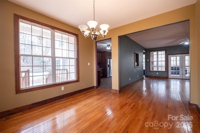 unfurnished room with light wood-style floors, baseboards, and ceiling fan with notable chandelier