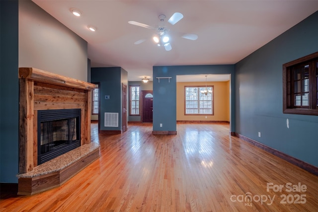 unfurnished living room featuring visible vents, a fireplace with raised hearth, baseboards, light wood-style flooring, and ceiling fan with notable chandelier