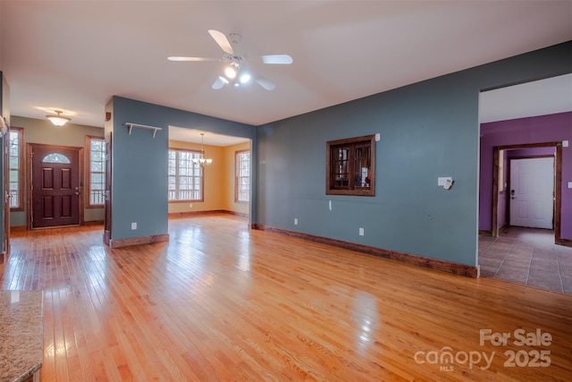 unfurnished living room featuring light wood-style floors, baseboards, and ceiling fan with notable chandelier