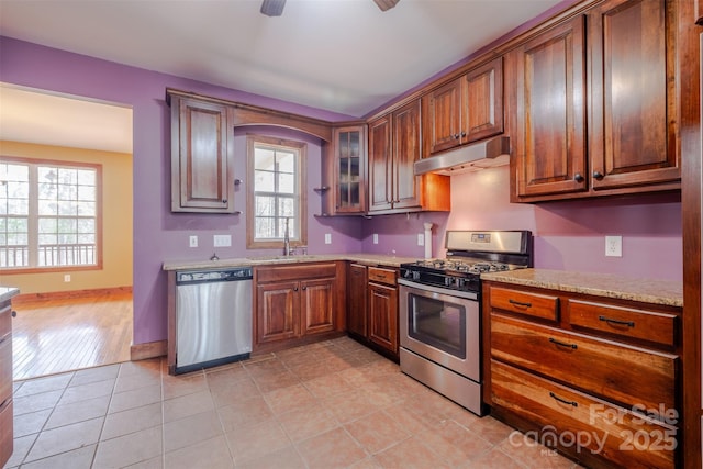 kitchen featuring light tile patterned floors, baseboards, appliances with stainless steel finishes, under cabinet range hood, and a sink