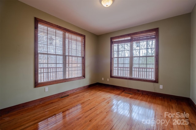 unfurnished room featuring a healthy amount of sunlight, visible vents, baseboards, and hardwood / wood-style flooring