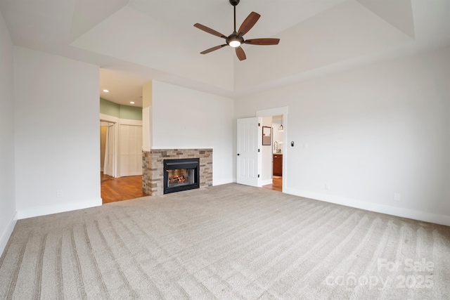 unfurnished living room with carpet, a tray ceiling, and a stone fireplace