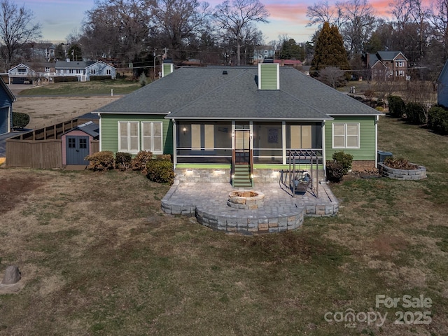 back house at dusk with a patio, a lawn, a storage shed, and a fire pit