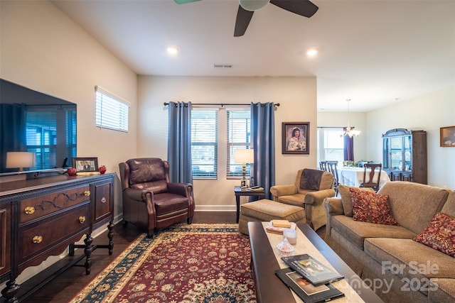 living room with dark wood-style floors, ceiling fan with notable chandelier, visible vents, and baseboards