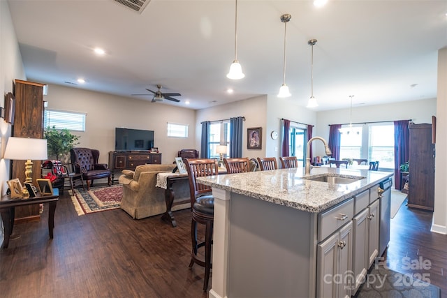 kitchen with a sink, gray cabinets, light stone countertops, a kitchen bar, and a center island with sink