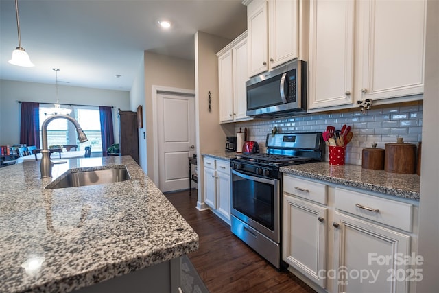 kitchen with stainless steel appliances, a sink, white cabinets, light stone countertops, and an island with sink