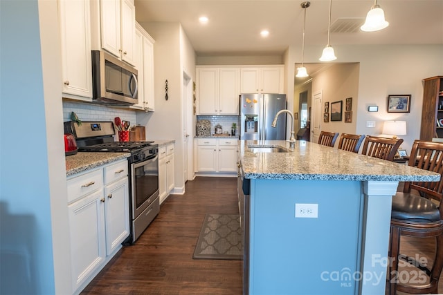 kitchen featuring stainless steel appliances, hanging light fixtures, a breakfast bar area, and a kitchen island with sink