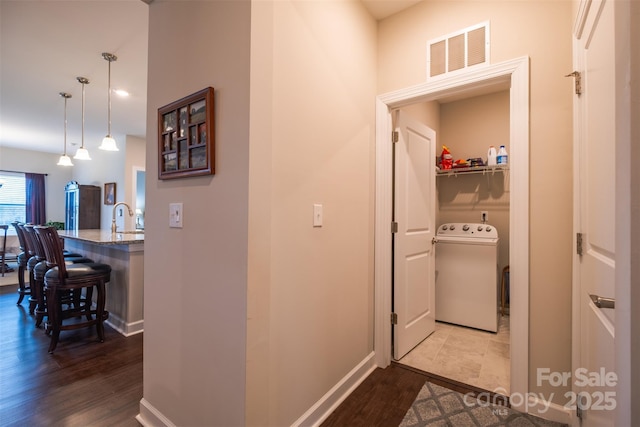 corridor with washer / dryer, baseboards, visible vents, wood finished floors, and a sink