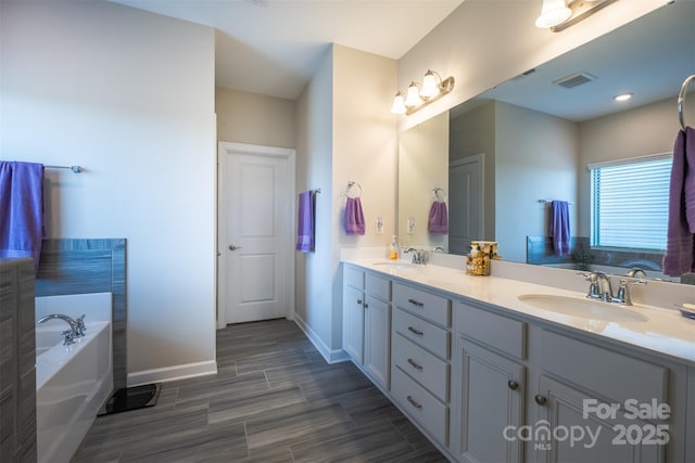 bathroom featuring a garden tub, double vanity, visible vents, a sink, and baseboards